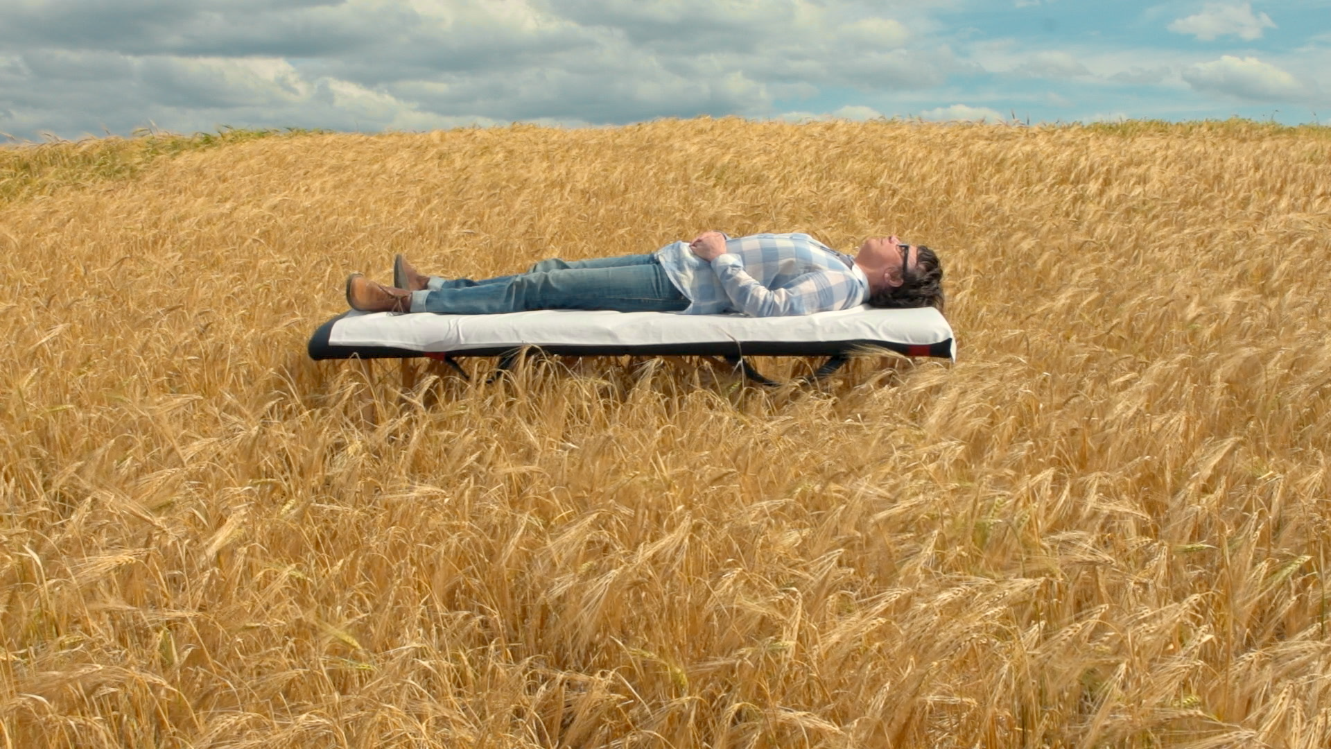 Image extraite du film « Chroniques hospitalières », une personne allongée sur un lit d’hôpital dans un champ de blé.