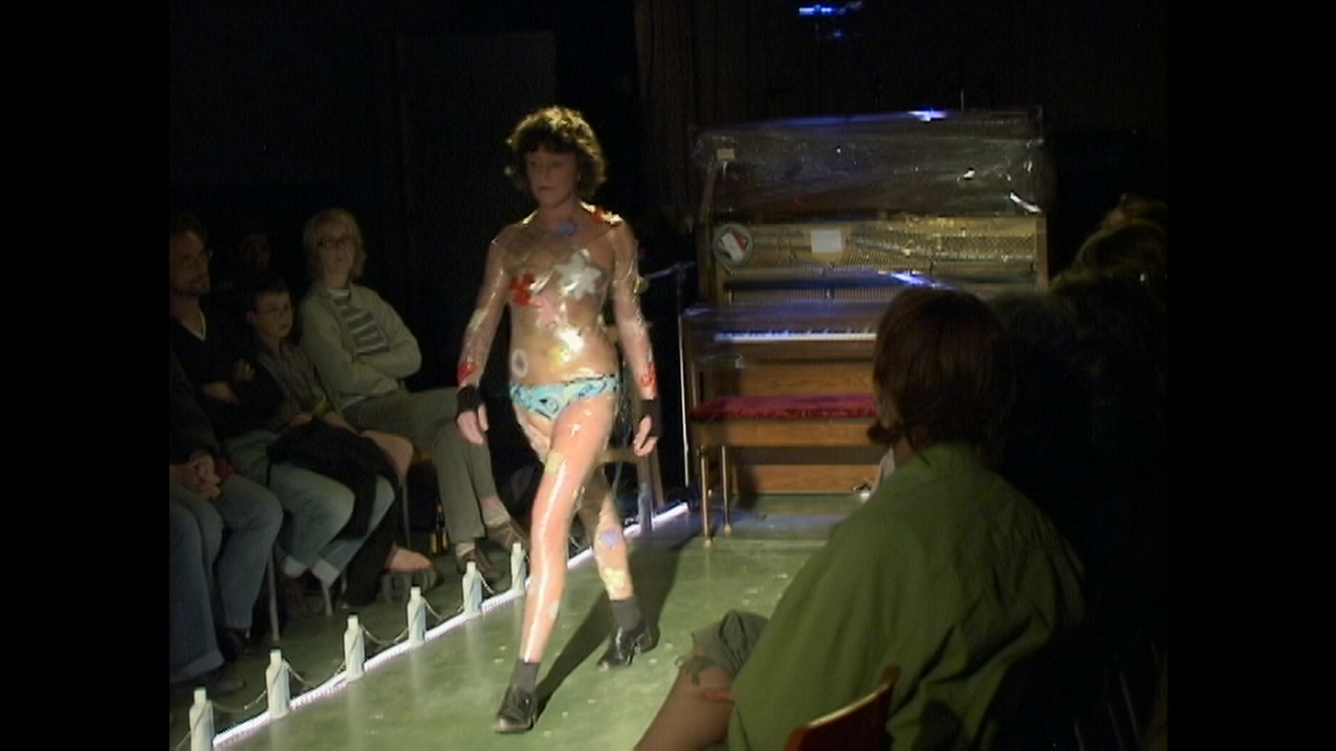 Image extraite du film « Chroniques hospitalières », une femme en sous-vêtements enveloppée de pellicule alimentaire marchant sur un podium.