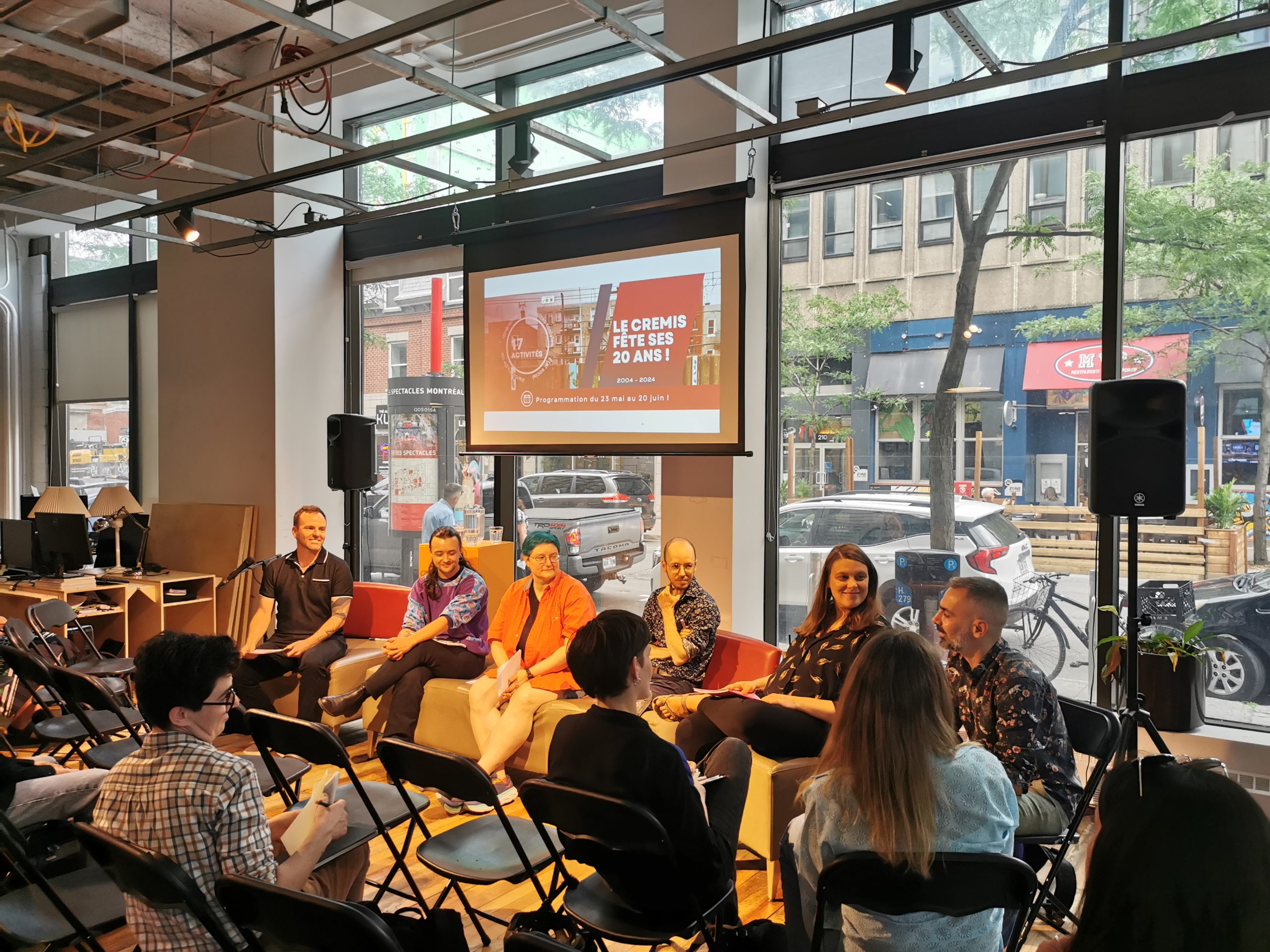 À l'espace ville autrement, lors de l'événement « Décloisonner les savoirs :  la recherche communautaire LGBTQ ». Vue sur les panélistes et sur la rue Sainte-Catherine en arrière, à travers une baie vitrée.