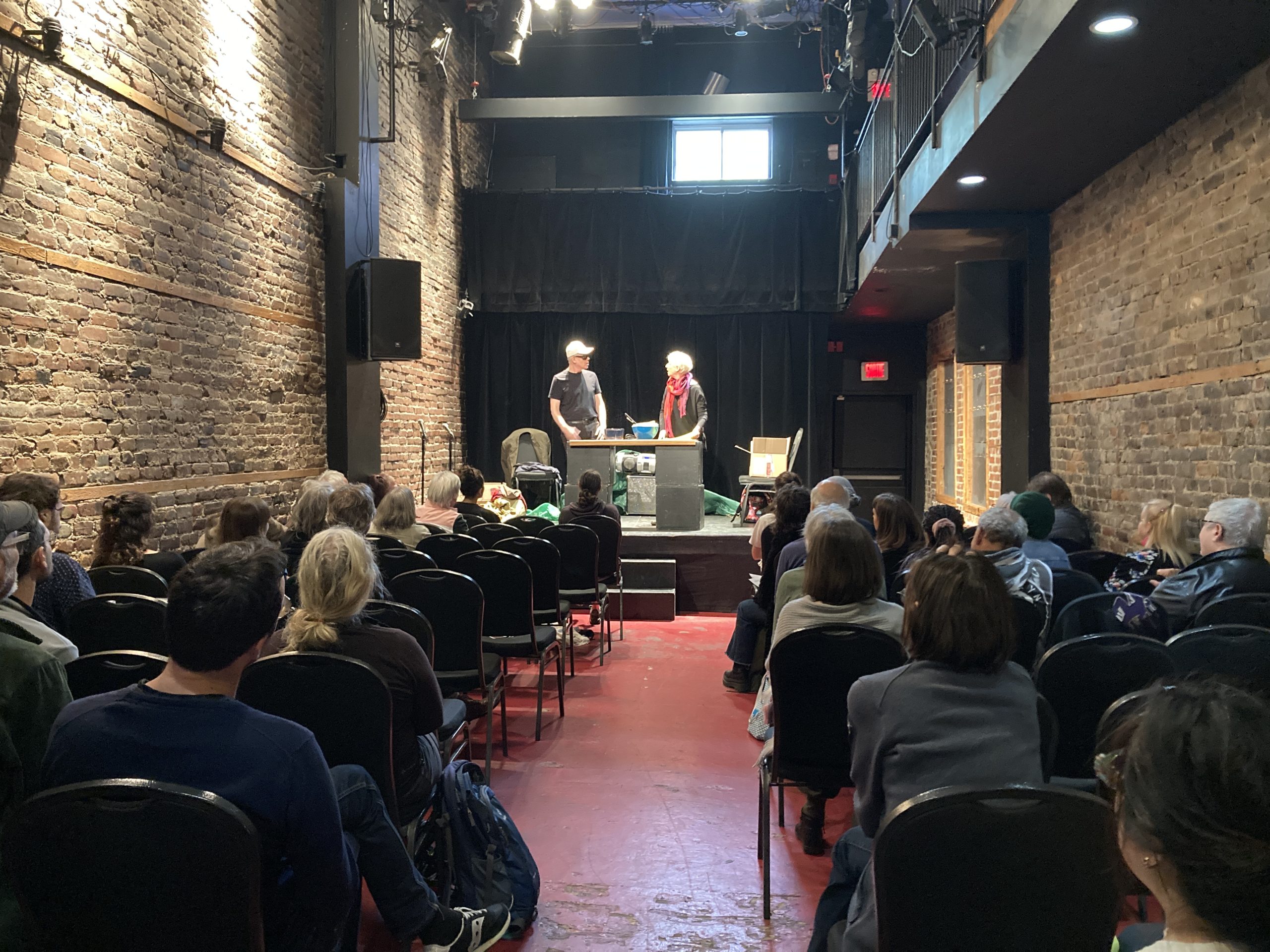 Au théâtre Sainte-Catherine, lors de le représentation de la pièce « Au delà du préjugé ». Vue du public de dos et des artistes sur scène.