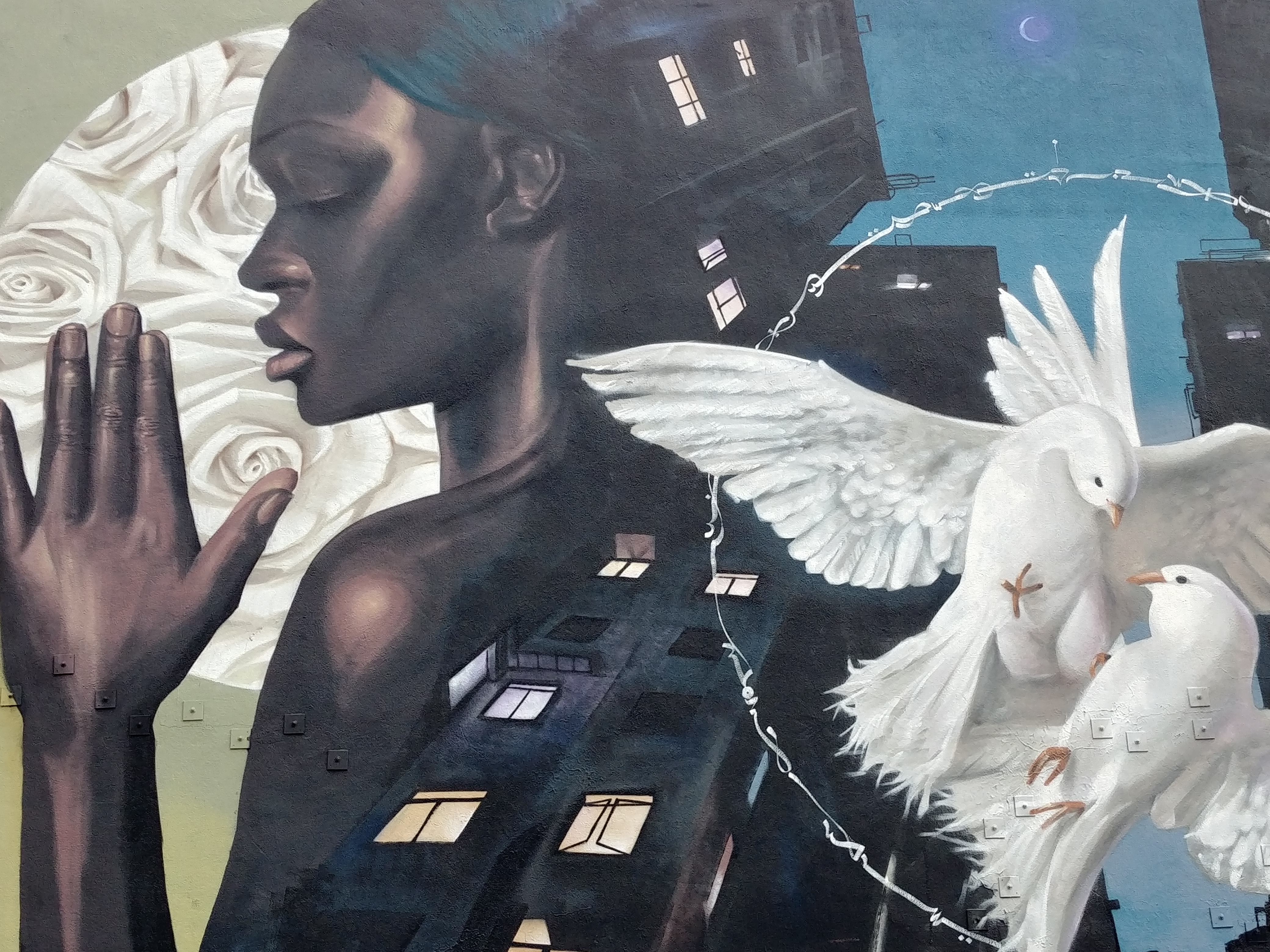 fresque murale représentant une femme noire devant des roses blanches, des bâtiments, deux colombes